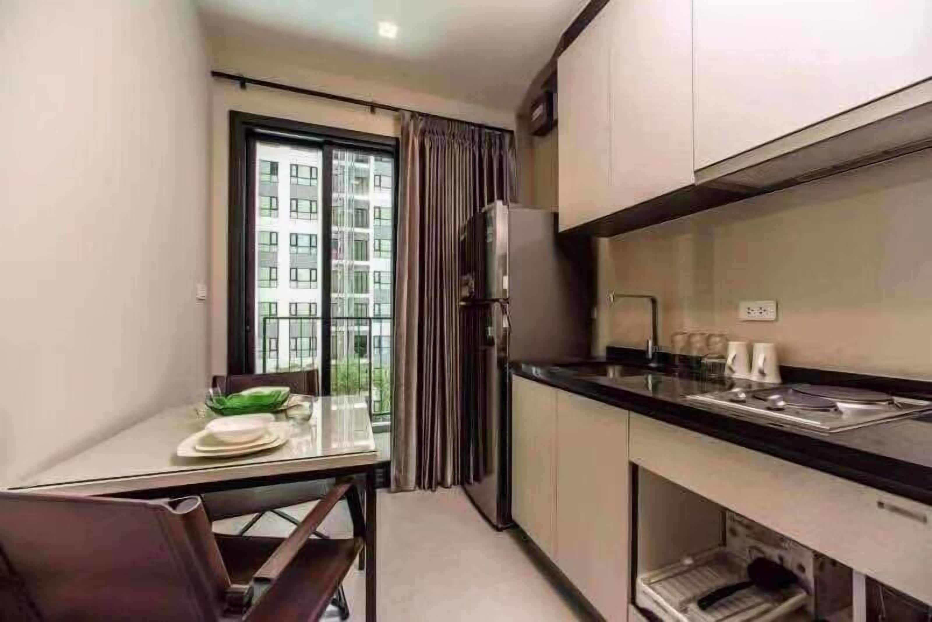 Una cocina compacta con comedor, refrigerador y ventana con cortinas.