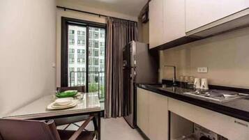 Una cocina compacta con comedor, refrigerador y ventana con cortinas.