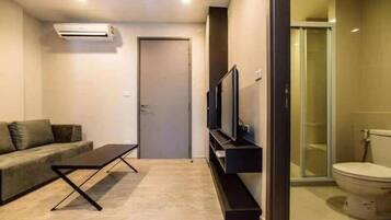 A modern living room with a sofa, a coffee table, a TV on a stand, and a glass shower enclosure.