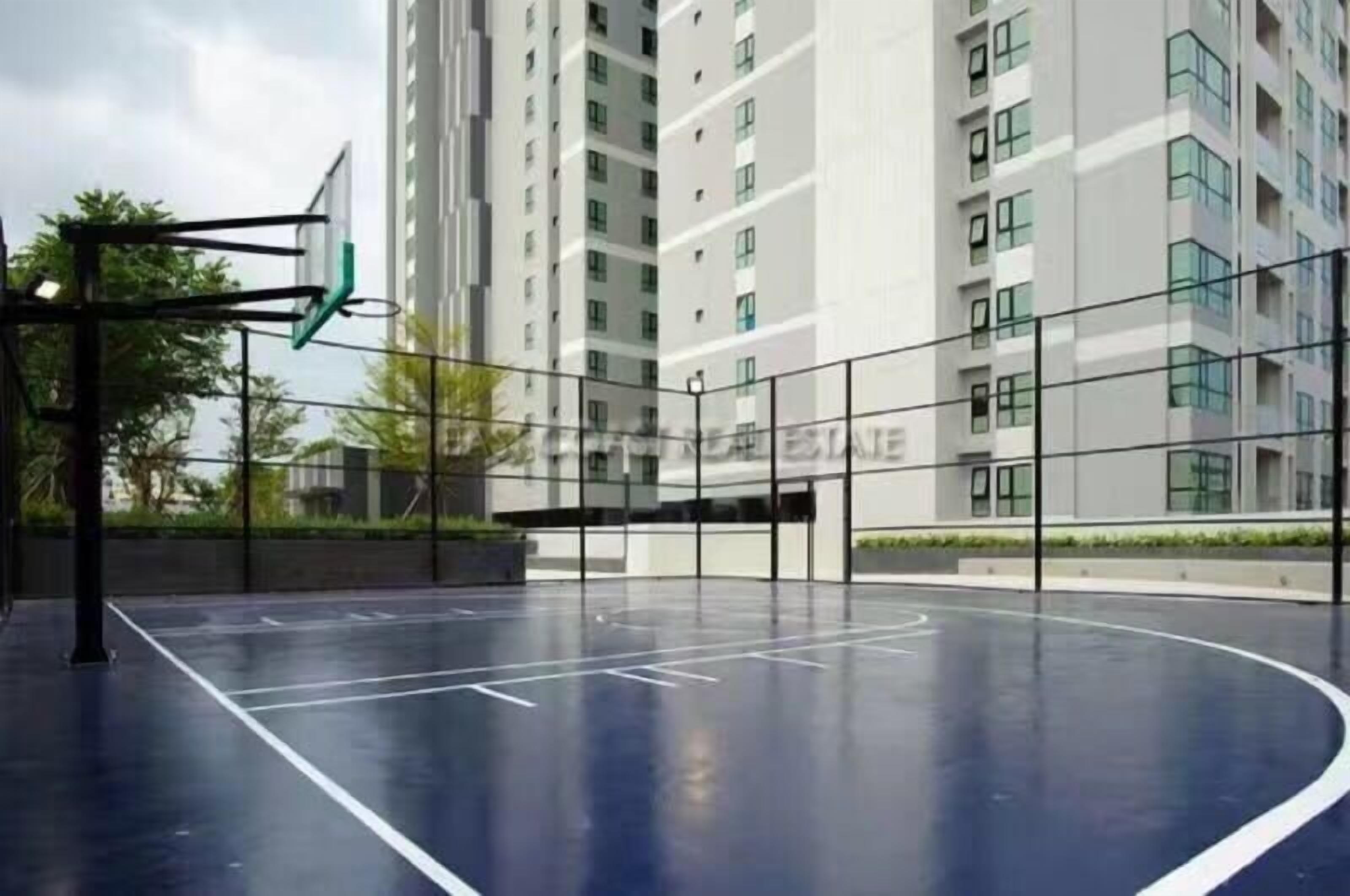 Eine überdachte Basketballhalle mit Korb, umzäunt und mit einem Gebäude im Hintergrund.