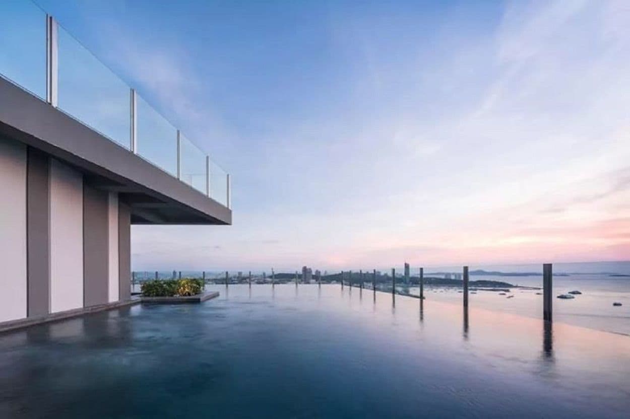 A modern building with a rooftop pool and a view of the city skyline at sunset.