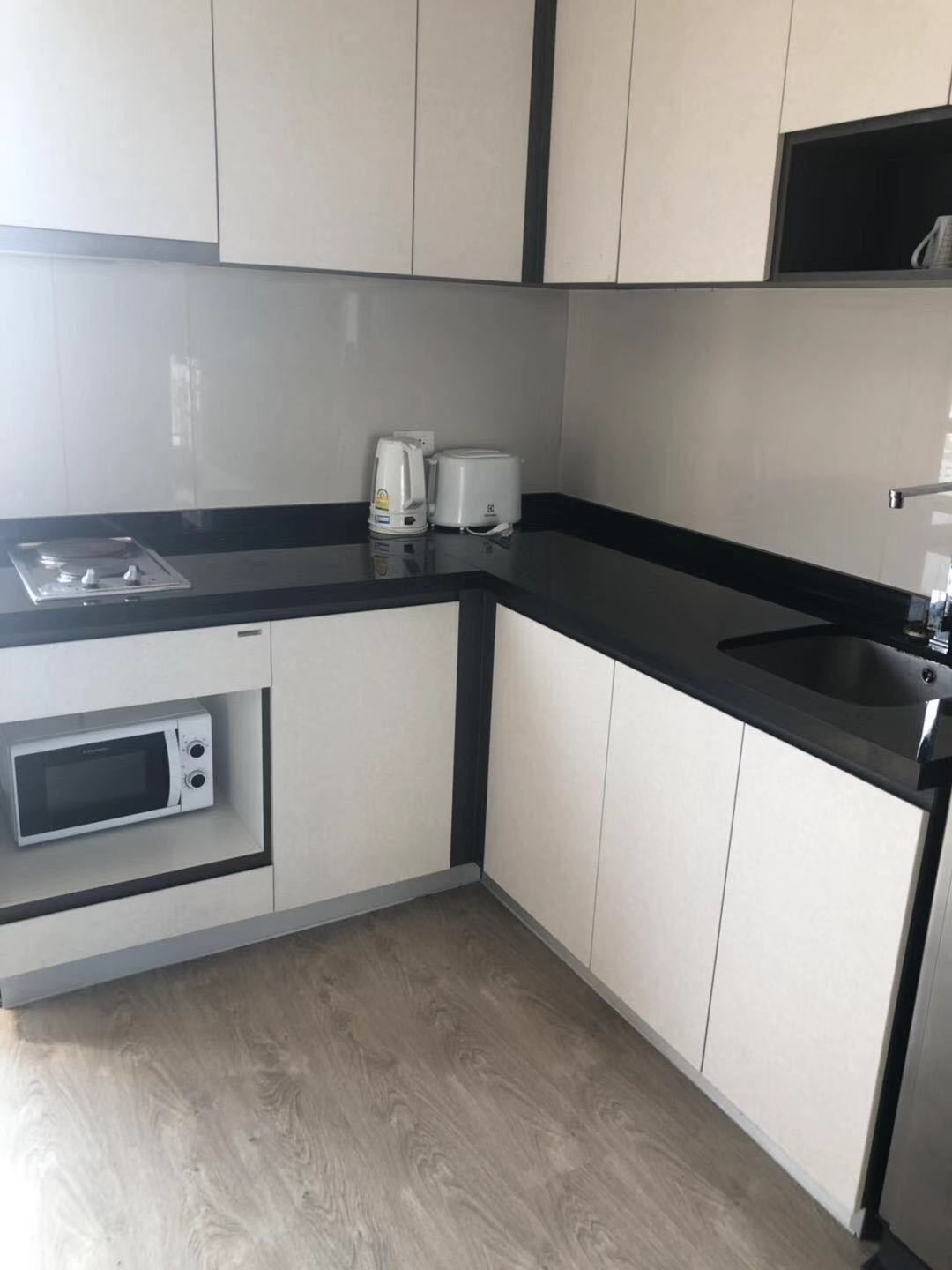 A kitchen with white cabinets, a black countertop, a microwave, a toaster, and a sink.