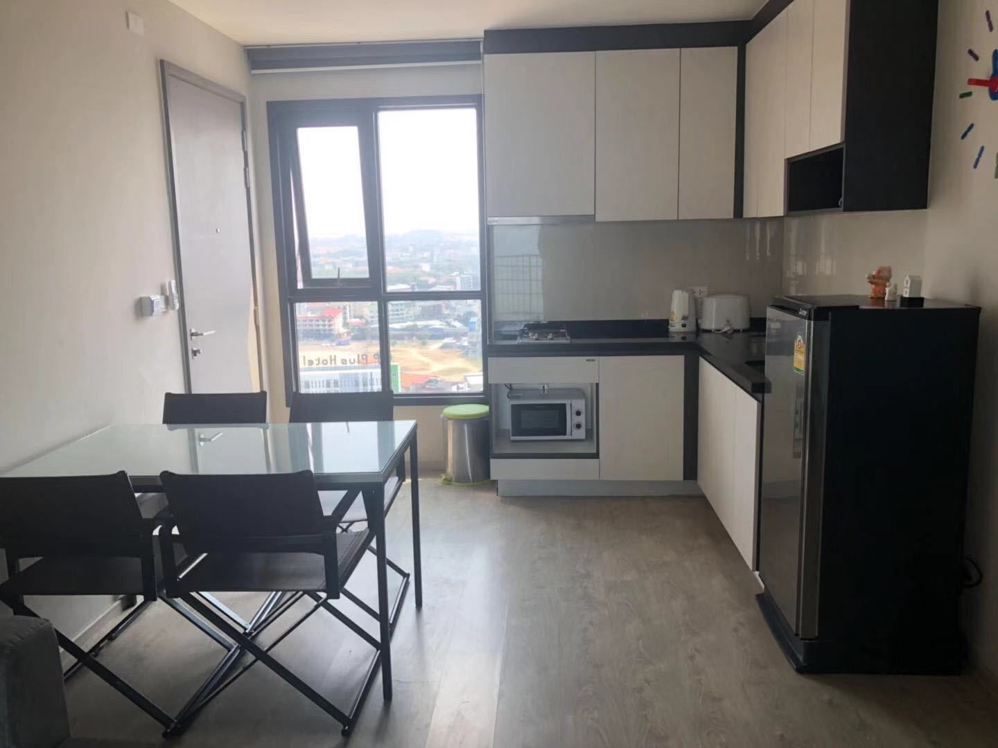 Eine moderne Küche mit Esstisch und Stühlen, einem Kühlschrank, einer Mikrowelle und einem Fenster mit Blick auf die Stadt.