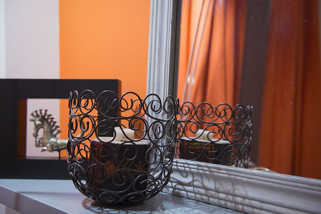 A metal candle holder on a windowsill with a reflection in the mirror.