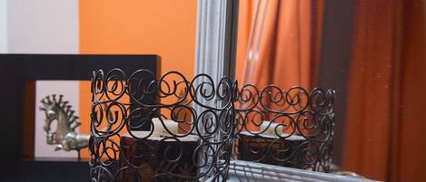 A metal candle holder on a windowsill with a reflection in the mirror.