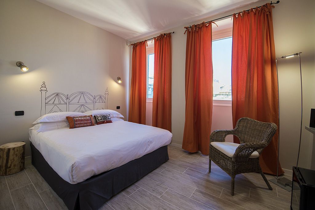 Une chambre à coucher avec un lit, des rideaux orange, un fauteuil en osier et une lampe sur pied.