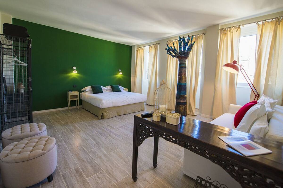 A hotel room with a green accent wall, a bed, a desk, a chair, and a lamp.