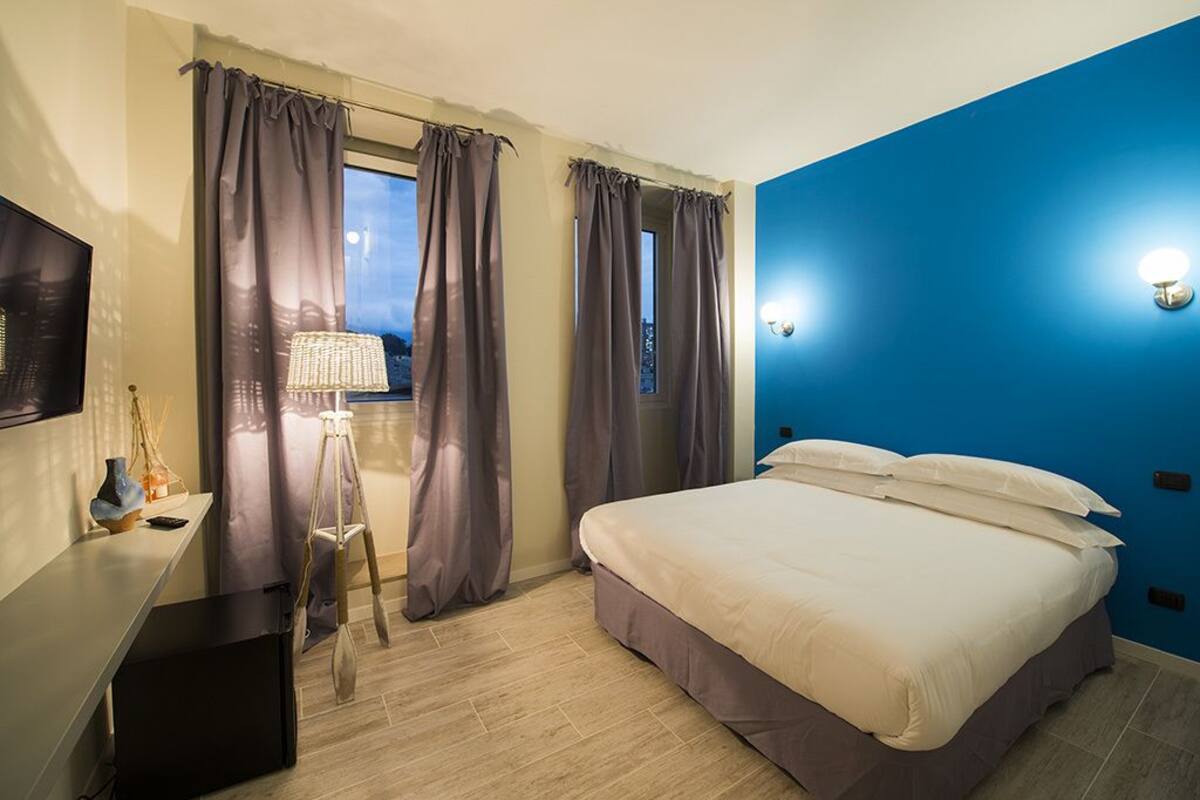 A hotel room with a bed, a desk, a lamp, and curtains.