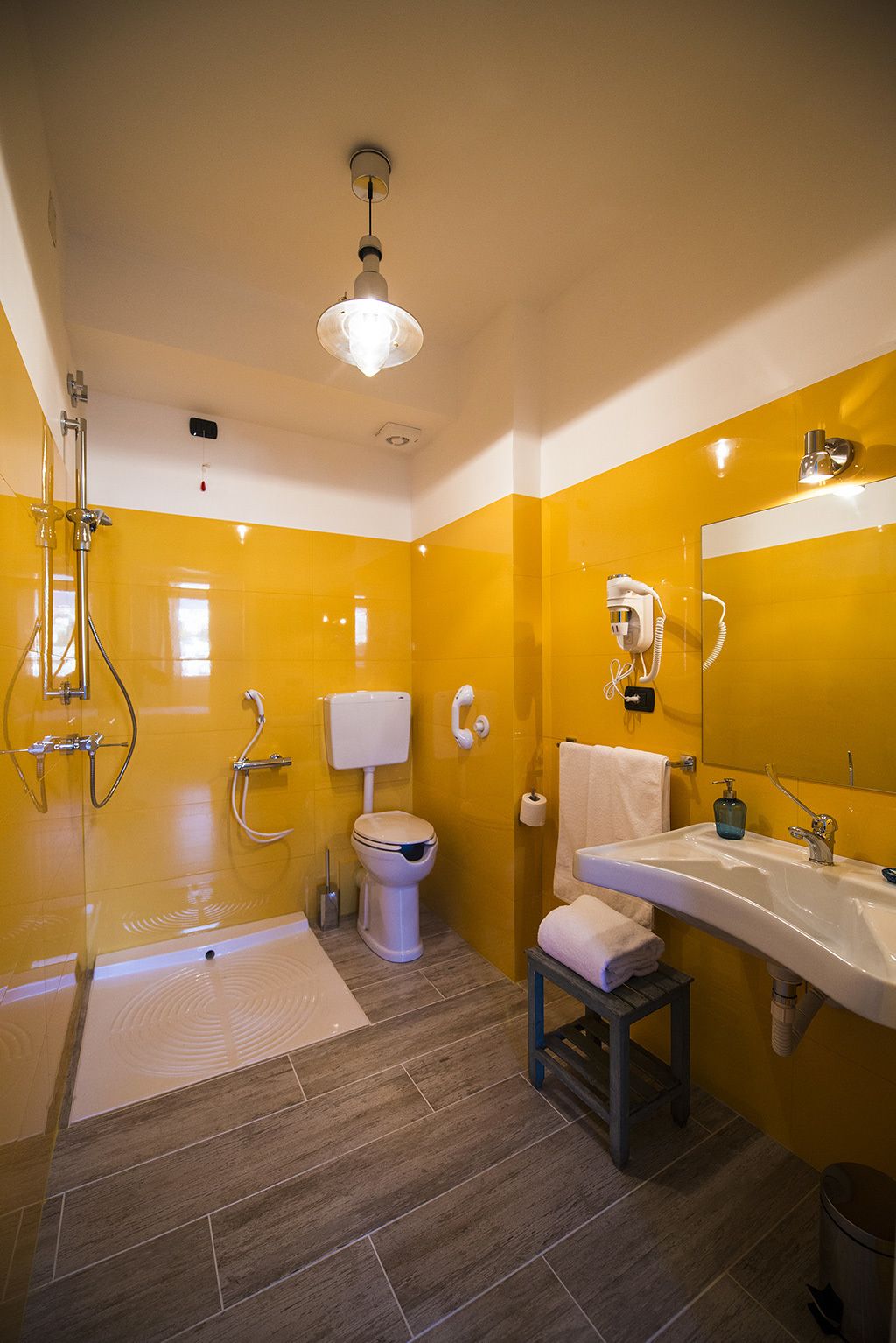 A modern bathroom with yellow walls, a white toilet, a shower with a glass enclosure, and a sink with a mirror above it.
