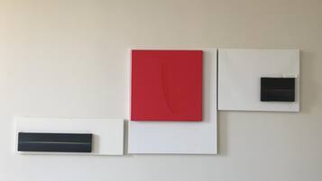 Un muro con tre opere d'arte incorniciate: un'opera rossa con un motivo curvo, un'opera nera con una linea orizzontale e un'opera bianca con un piccolo rettangolo nero.