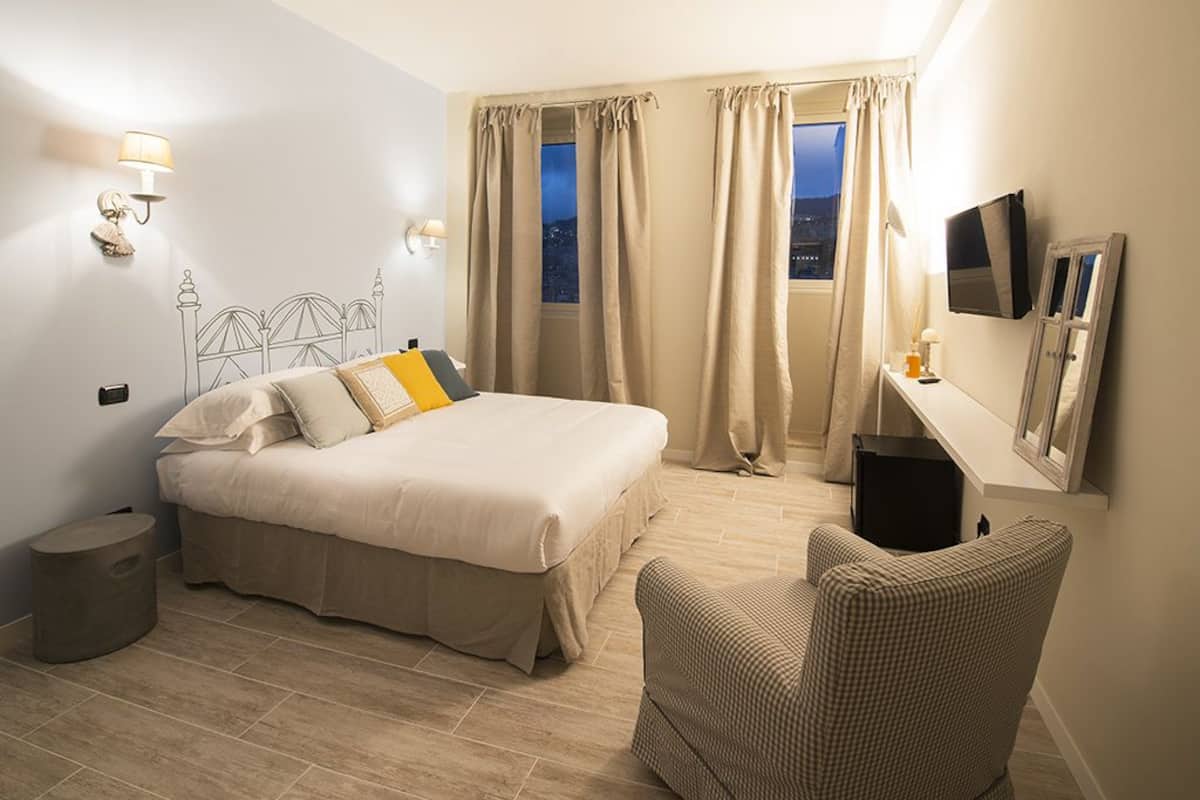 A hotel room with a bed, a chair, a TV, and a window with curtains.