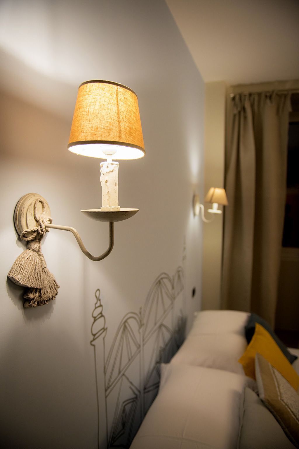A wall-mounted lamp with a textured shade, a decorative tassel, and a geometric wall design.