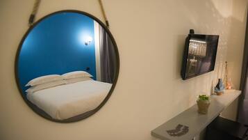 A room with a bed, a round mirror, a flat-screen TV, and a small shelf with decorative items.