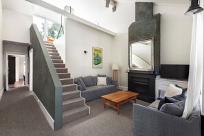 Ein modernes Wohnzimmer mit Treppe, grauen Sofas, einem Holztisch, einem Kamin und einem Fernseher.