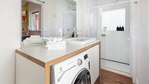 Un baño moderno con lavadora integrada, un espejo grande y zona de ducha.