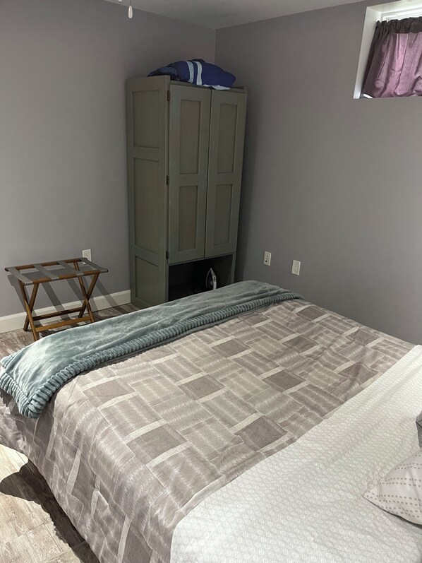 Ein Schlafzimmer mit Bett, Schrank, einem kleinen Tisch und einem Fenster mit Vorhängen.