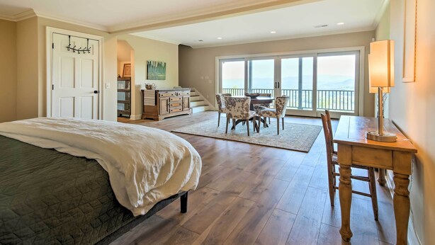 A bedroom with a large bed, a desk with a chair, a dining area with chairs, and a view of the outdoors through a large window. - Hiawassee Getaway w/ Deck, Mountain & Lake Views! (Hiawassee)