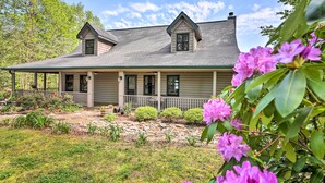 A two-story house with a covered porch, stone foundation, and a well-maintained garden with flowering plants. - Hiawassee Getaway w/ Deck, Mountain & Lake Views! (Hiawassee)