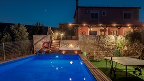 A swimming pool with a stone wall and a wooden deck, a hot tub, and a covered patio area with string lights. - Villa Elise, Beautiful house, A/C, Private Pool, Table Tennis . (Kokkini Hani, Heraklion, Crete)