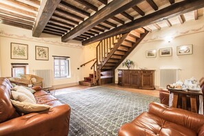 A spacious living room with a high wooden ceiling, a staircase, and a view of the outdoors.