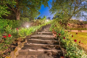 A stone staircase surrounded by lush greenery and red flowers, leading up a hill.