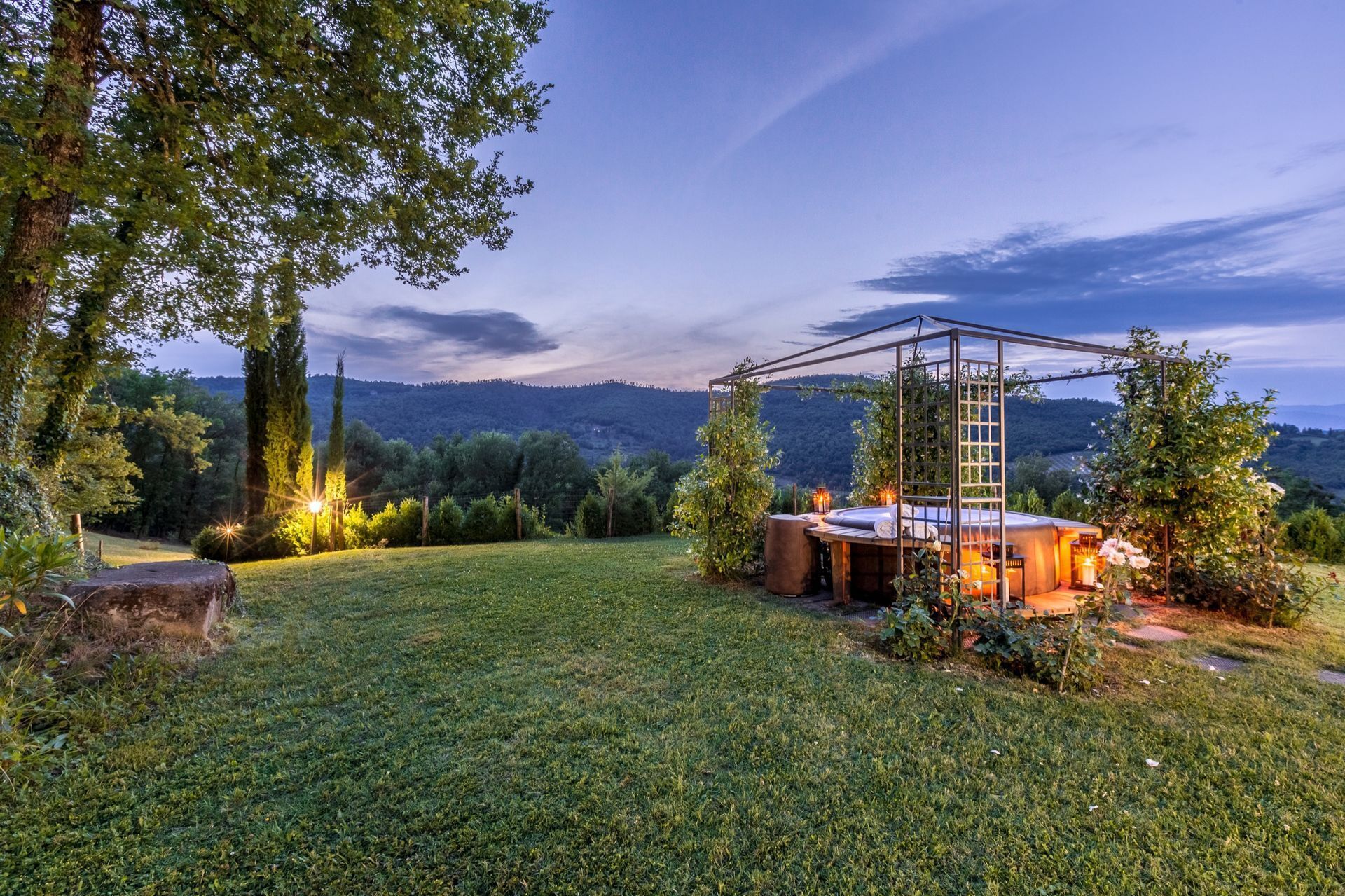 Zona d'estar a l'exterior amb un ambient rural, amb una estructura de pergola, envoltada de vegetació abundant i vistes a les muntanyes llunyanes.