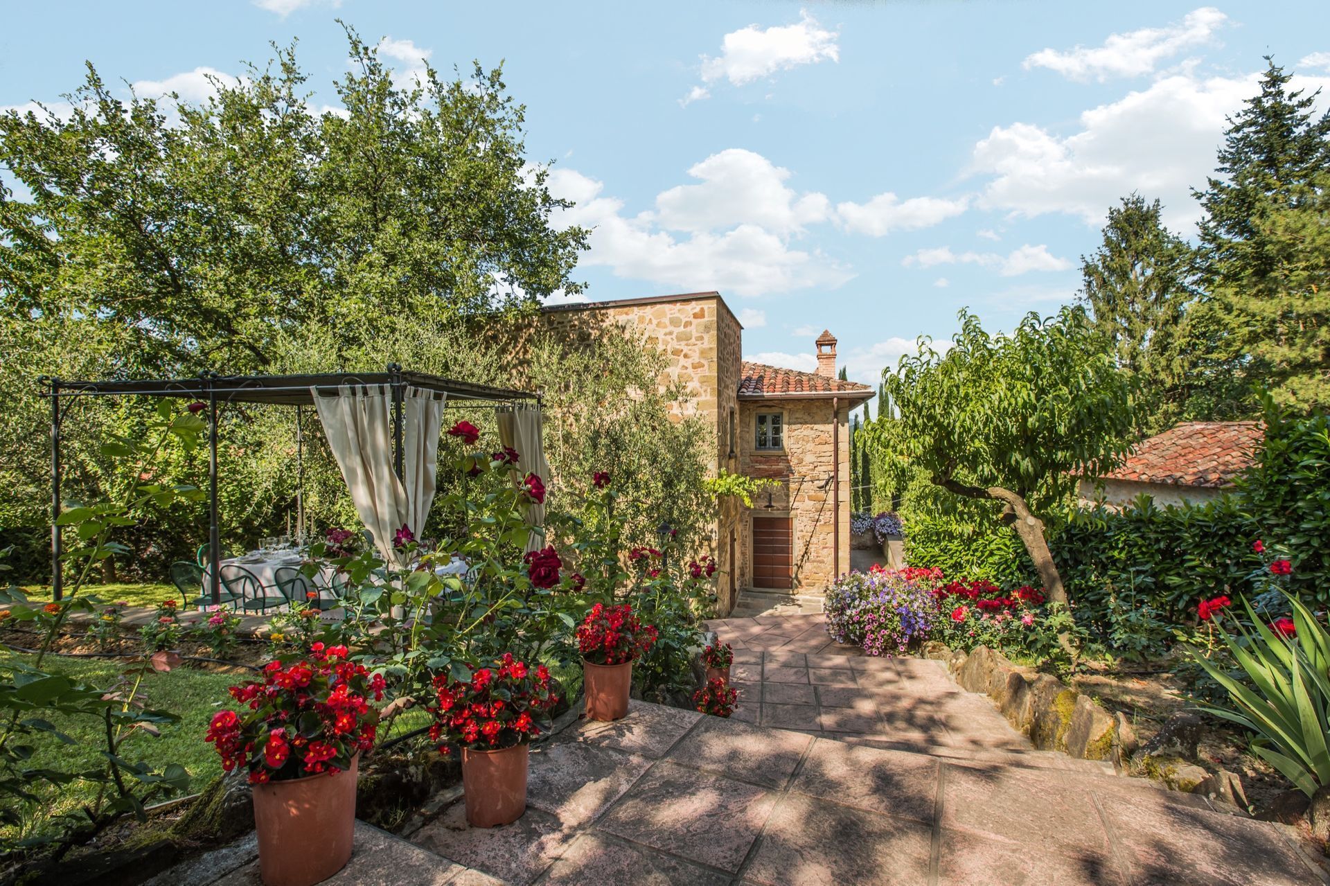 A stone building with a tiled roof, surrounded by lush greenery and potted plants.