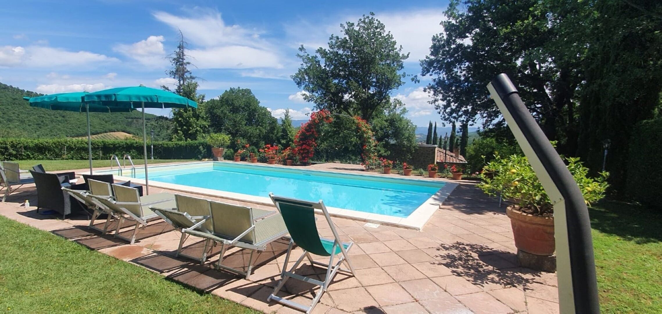 A rectangular swimming pool with a tiled deck, surrounded by lounge chairs and a green umbrella.