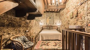 A rustic bedroom with a stone wall, wooden beams, a bed with a patterned headboard, and a woven chair. - Stunning private villa with WIFI, hot tub, private pool, A/C, TV, patio and panoramic view (Monterchi)