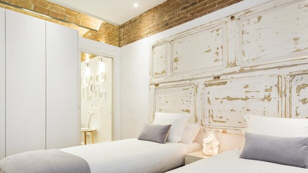 Un dormitorio con dos camas, una pared de ladrillo y una puerta blanca.