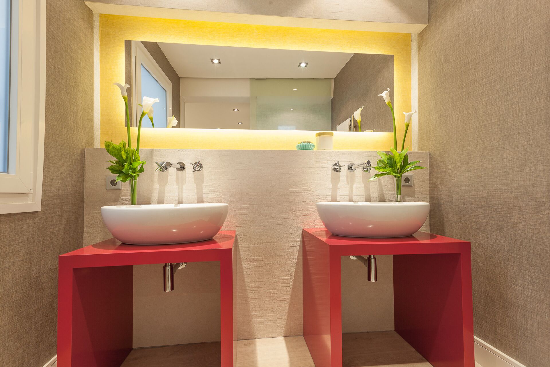 A modern bathroom with two white vessel sinks on red pedestals, a yellow accent wall, and a mirror above.