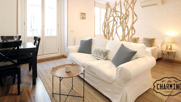 A living room with a white sofa, a small round table, and a dining area with a table and chairs. - Huertas studio - Apartment in the center of Madrid (Madrid)
