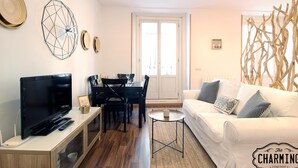 A modern living room with a flat-screen TV, a dining table with chairs, a white sofa with patterned cushions, and a decorative wall piece. - Huertas studio - Apartment in the center of Madrid (Madrid)