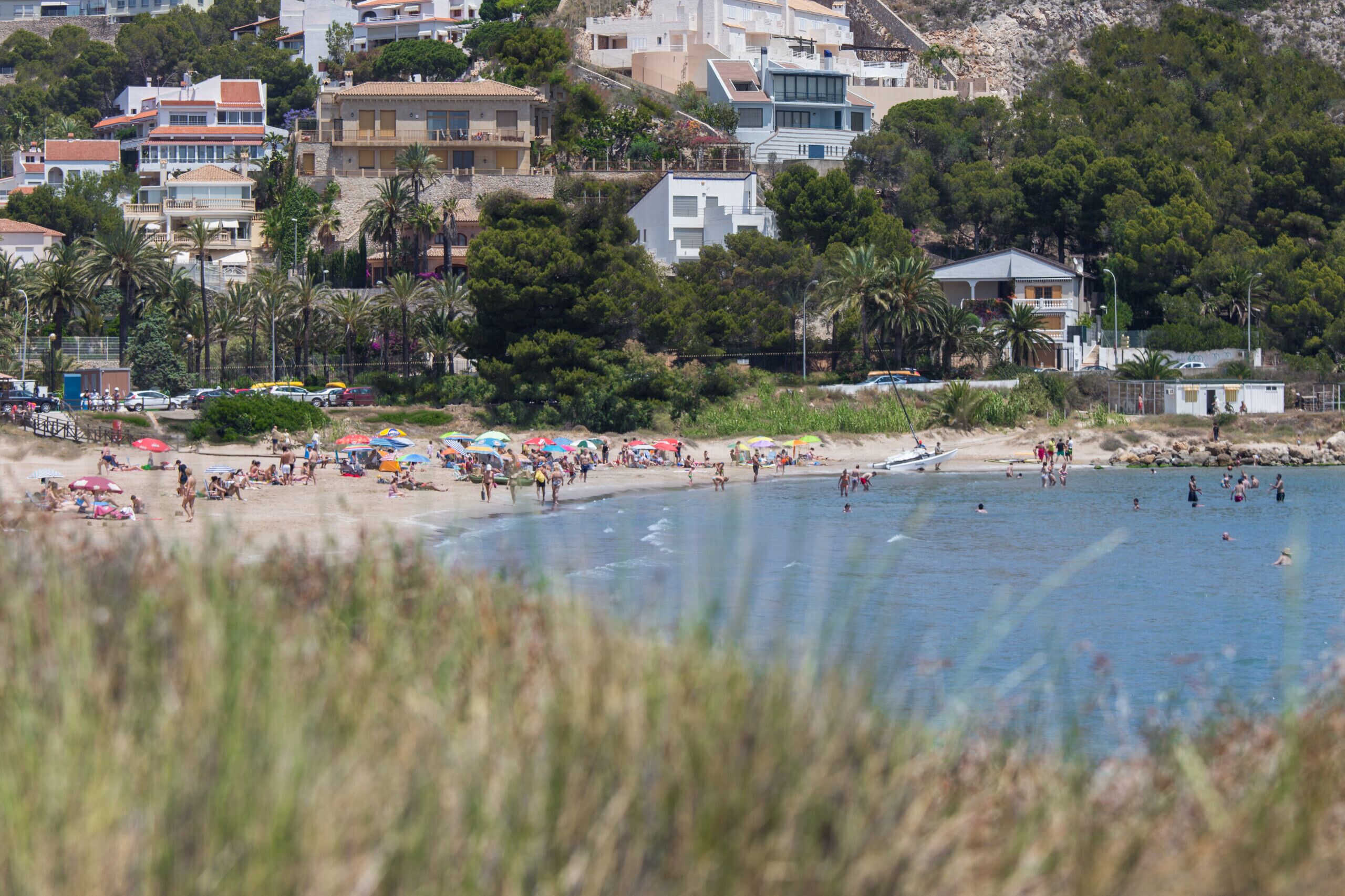 A beach with people sunbathing and swimming, surrounded by buildings and trees.