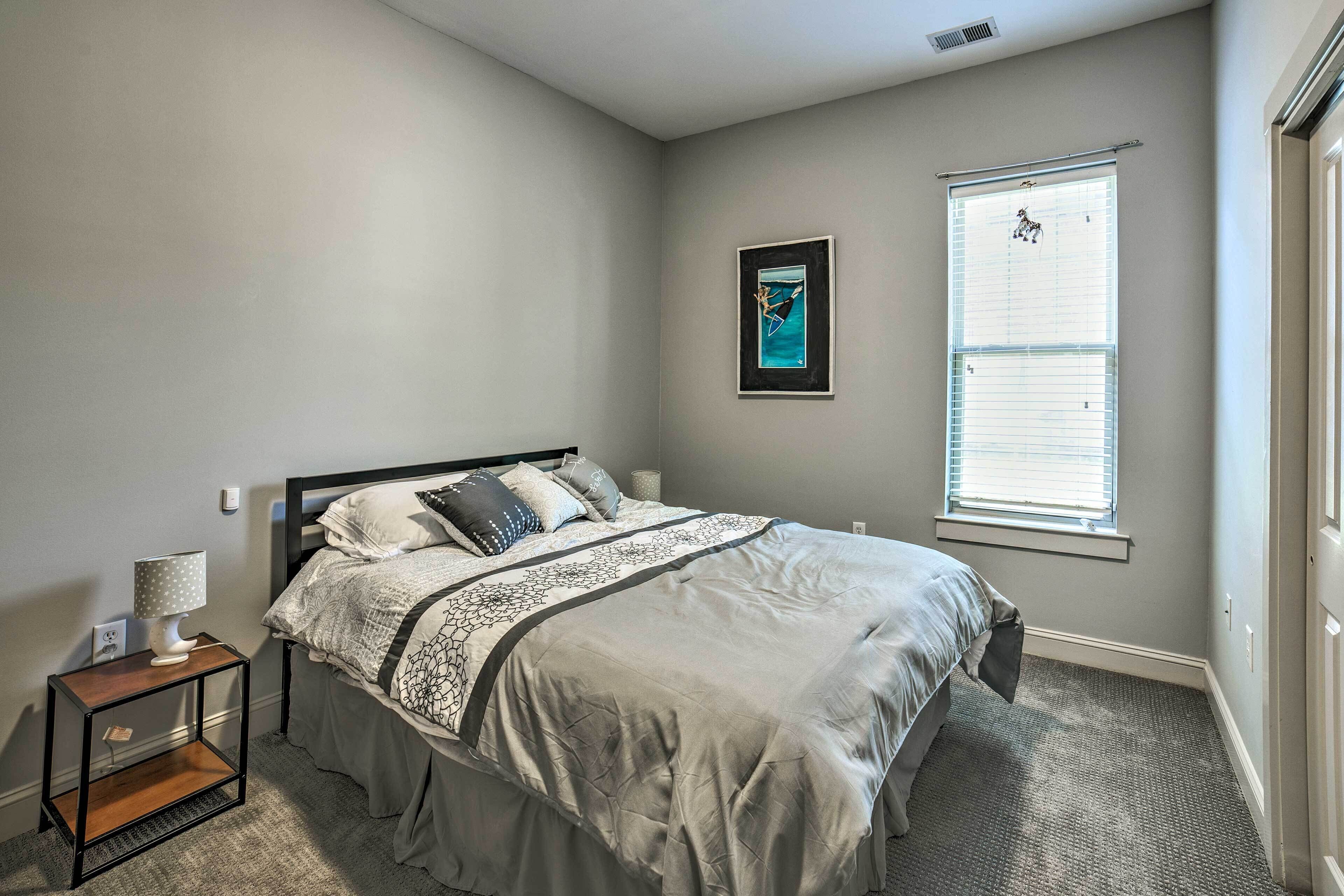 A bedroom with a bed, a nightstand, a window with blinds, and a framed picture on the wall.