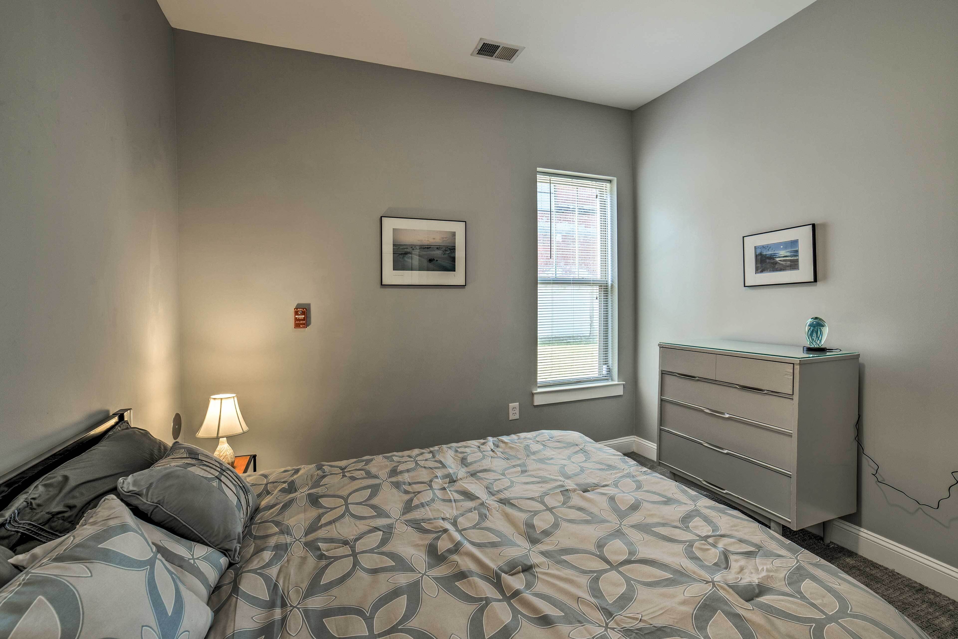 A bedroom with a bed, dresser, nightstand, lamp, and two framed pictures on the wall.