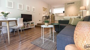 Uma sala de estar moderna com televisão de tela plana, área de jantar com mesa e cadeiras, sofá, pequena mesa lateral e ventilador de teto.
