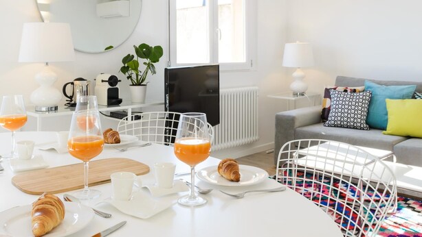 Un salon moderne avec un coin repas, des meubles blancs, un téléviseur et une fenêtre.