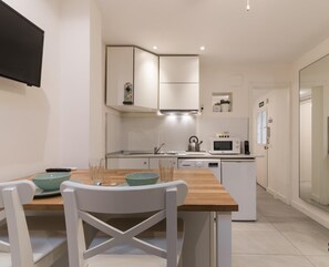 Une cuisine moderne avec des meubles blancs, une table à manger en bois et un micro-ondes encastré.