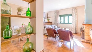 Un salón con sofá, sillas, chimenea y estanterías con botellas de vidrio verde.