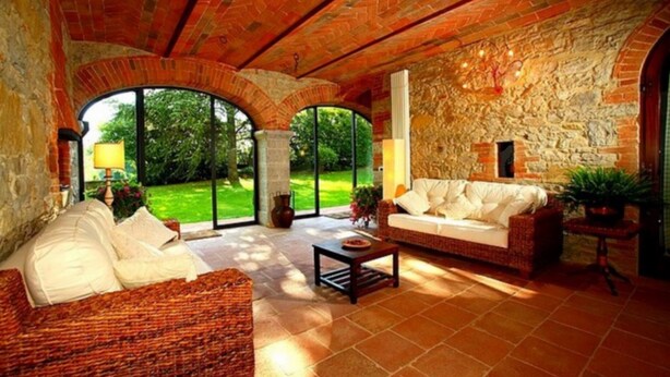 A spacious living room with a high ceiling, stone walls, and large windows offering a view of a lush garden. - Podere Lucignano Secondo Agriturismo (Gaiole in Chianti)