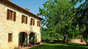 A stone building with arched doorways and wooden shutters, surrounded by a well-maintained lawn and trees. - Podere Lucignano Secondo Agriturismo (Gaiole in Chianti)