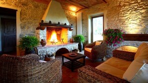 A cozy room with a stone fireplace, wicker furniture, and a large window. - Podere Lucignano Secondo Agriturismo (Gaiole in Chianti)