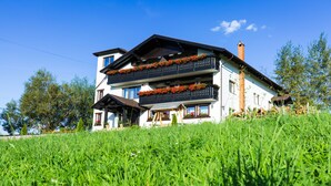 A two-story building with balconies adorned with flowers, set on a grassy hill. - Branmontecrai (Bran)