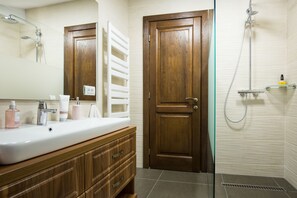 A bathroom with a wooden vanity, a white sink, and a shower area. - Branmontecrai (Bran)