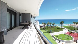 A balcony with a dining table and chairs, overlooking a pool area with palm trees and a view of the ocean. - Luxurious apartment in Elche with sauna (Elche)