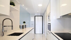 A modern kitchen with white cabinetry, a stainless steel sink, and a black countertop. - Luxurious apartment in Elche with sauna (Elche)