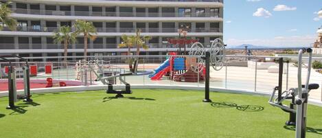 Gimnasio en la azotea con equipamiento de ejercicio y zona de juegos infantiles.