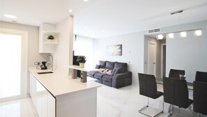 A modern kitchen with a white countertop, a gray sofa, and a dining area with black chairs. - Luxurious apartment in Elche with sauna (Elche)