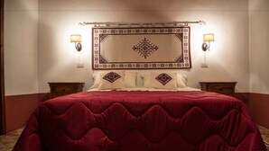 Una cama con colcha roja, dos lámparas de pared y un cabecero decorativo.